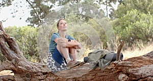 Young Caucasian woman sits on a fallen tree, looking thoughtful