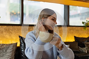Young caucasian woman sitting in cafeteria holding coffee mug while looking away. Middle aged woman drinking tea in cafe
