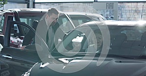 Young Caucasian woman sitting in car and talking with dealer. Trader helping customer to choose vehicle in dealership