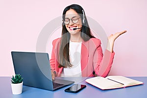 Young caucasian woman sitting at the desk wearing call center agent headset working using laptop celebrating victory with happy
