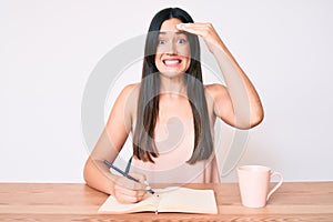 Young caucasian woman sitting at the desk writing book drinking coffee stressed and frustrated with hand on head, surprised and