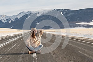 Young caucasian woman sitting on empty road against mountains