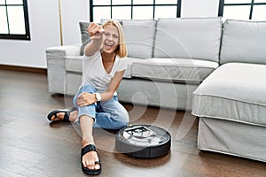 Young caucasian woman sitting at home by vacuum robot pointing displeased and frustrated to the camera, angry and furious with you