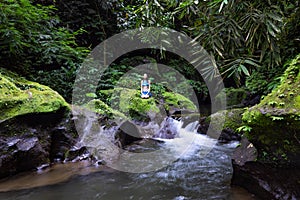 Young Caucasian woman sitting on the rock near the river in Vajrasana or Diamond pose. Hands in gyan mudra. Tropical nature