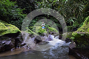 Young Caucasian woman sitting on the rock near the river in Vajrasana or Diamond pose. Hands in namaste mudra. Tropical nature