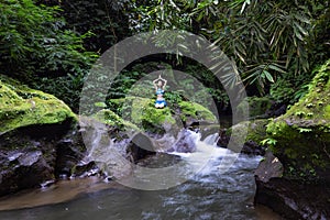 Young Caucasian woman sitting on the rock near the river in Vajrasana or Diamond pose. Hands raising up in namaste mudra. Tropical