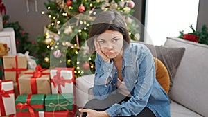 Young caucasian woman sitting on sofa by christmas tree looking upset at home