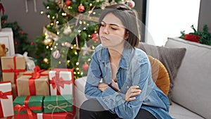 Young caucasian woman sitting on sofa by christmas tree looking upset at home