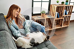 Young caucasian woman sitting on sofa playing with dog at home