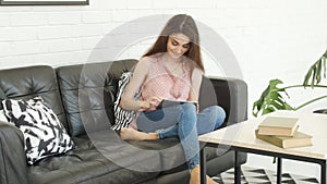 Young caucasian woman sitting on sofa and using tablet pc