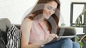 Young caucasian woman sitting on sofa and using tablet pc