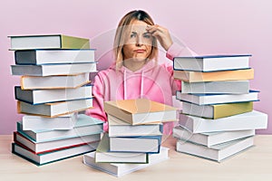 Young caucasian woman sitting on the table with books worried and stressed about a problem with hand on forehead, nervous and