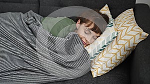 Young caucasian woman sleeping on the sofa covered with blanket at home