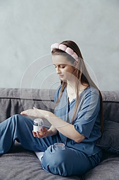 Young Caucasian woman in a sleepwear hydrates her skin using a moisturizing lotion from a jar
