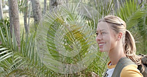 A young Caucasian woman smiles while exploring a lush outdoor setting with copy space