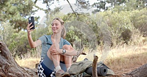 A young Caucasian woman smiles while looking at her smartphone outdoors