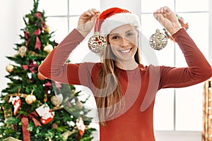 Young caucasian woman smiling confident holding christmas balls decor at home