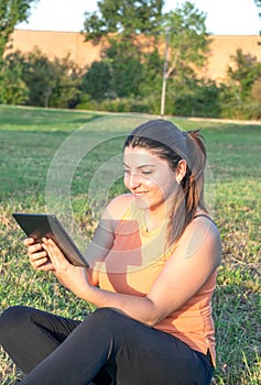 Young Caucasian woman smiling and happy using tablet sitting in park