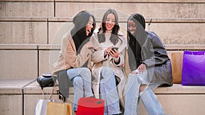 Young caucasian woman smiling and having fun showing a sale on the smart phone to her multiracial friends in a shopping