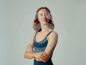 Young caucasian woman in sports bra looking over shoulder with arms crossed in studio