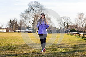 A young Caucasian woman in sportswear with a backpack behind her is walking on the lawn. The concept of sport and active life