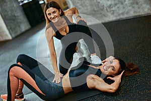 Young caucasian woman in sportswear and her personal trainer or fitness instructor smiling at camera while exercising at