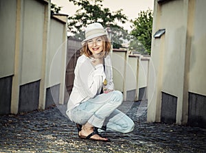 Young caucasian woman squats in the ancient street on the castle