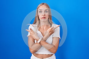 Young caucasian woman standing over blue background pointing to both sides with fingers, different direction disagree