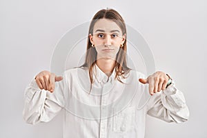 Young caucasian woman standing over isolated background pointing down looking sad and upset, indicating direction with fingers,