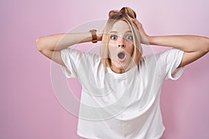 Young caucasian woman standing over pink background crazy and scared with hands on head, afraid and surprised of shock with open
