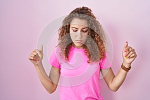 Young caucasian woman standing over pink background pointing down looking sad and upset, indicating direction with fingers,