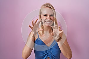 Young caucasian woman standing over pink background smiling funny doing claw gesture as cat, aggressive and sexy expression