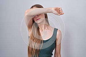 Young caucasian woman standing over white background covering eyes with arm, looking serious and sad