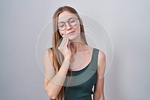 Young caucasian woman standing over white background touching mouth with hand with painful expression because of toothache or