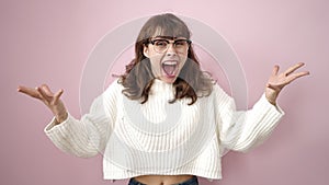 Young caucasian woman standing with surprise expression and raised arms over isolated pink background