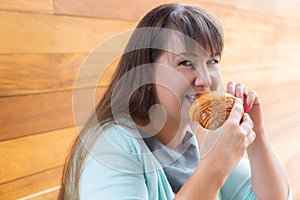 Young Caucasian woman with straight hair eating croissant in a coffee shop