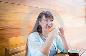 Young Caucasian woman with straight hair eating croissant in a coffee shop