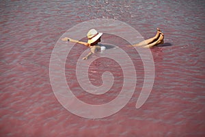 Young caucasian woman in a straw hat floating in a pink salty Lemuriysk Syvash lake, Ukraine.