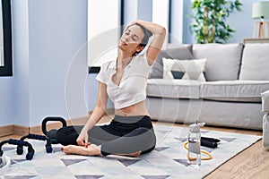 Young caucasian woman stretching head sitting on floor at home