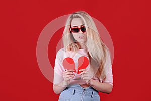 Young caucasian woman in sunglasses with broken red heart in hands.