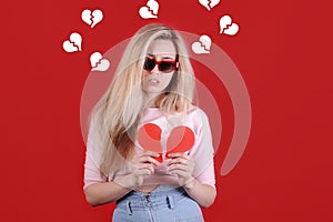 Young caucasian woman in sunglasses with broken red heart in hands.