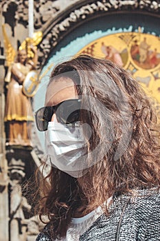 Young Caucasian woman with sunglasses and medical face mask photographed in front of the Astronomical clock Orloj in Prague, Czech