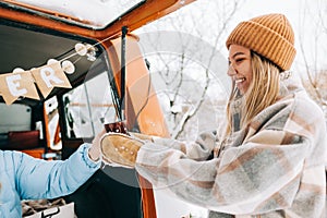 Young caucasian woman taking mug with hot tea near van , in winter time outdoor, during road trip