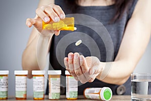 A young caucasian woman is taking a pill out of the medication bottle