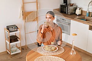 Young caucasian woman taking sip of water during dinner of home cooked pasta, sitting at table in kitchen, above view