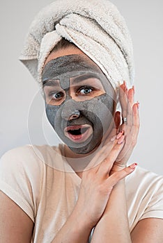 young caucasian woman in towel on head with black clay or mud facial mask isolated on white