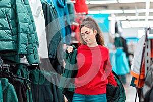 A young Caucasian woman tries on a winter jacket in a store. The concept of shopping and consumerism