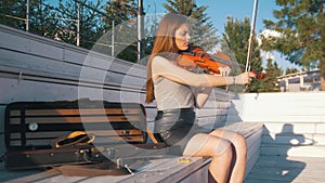 Young caucasian woman tunes her violin sitting on the bench in summer park