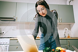 Young caucasian woman use tablet computer in the modern kitchen, preparing salad, read recipe