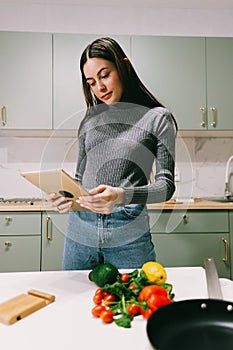 Young caucasian woman use tablet computer in the modern kitchen, preparing salad, read recipe